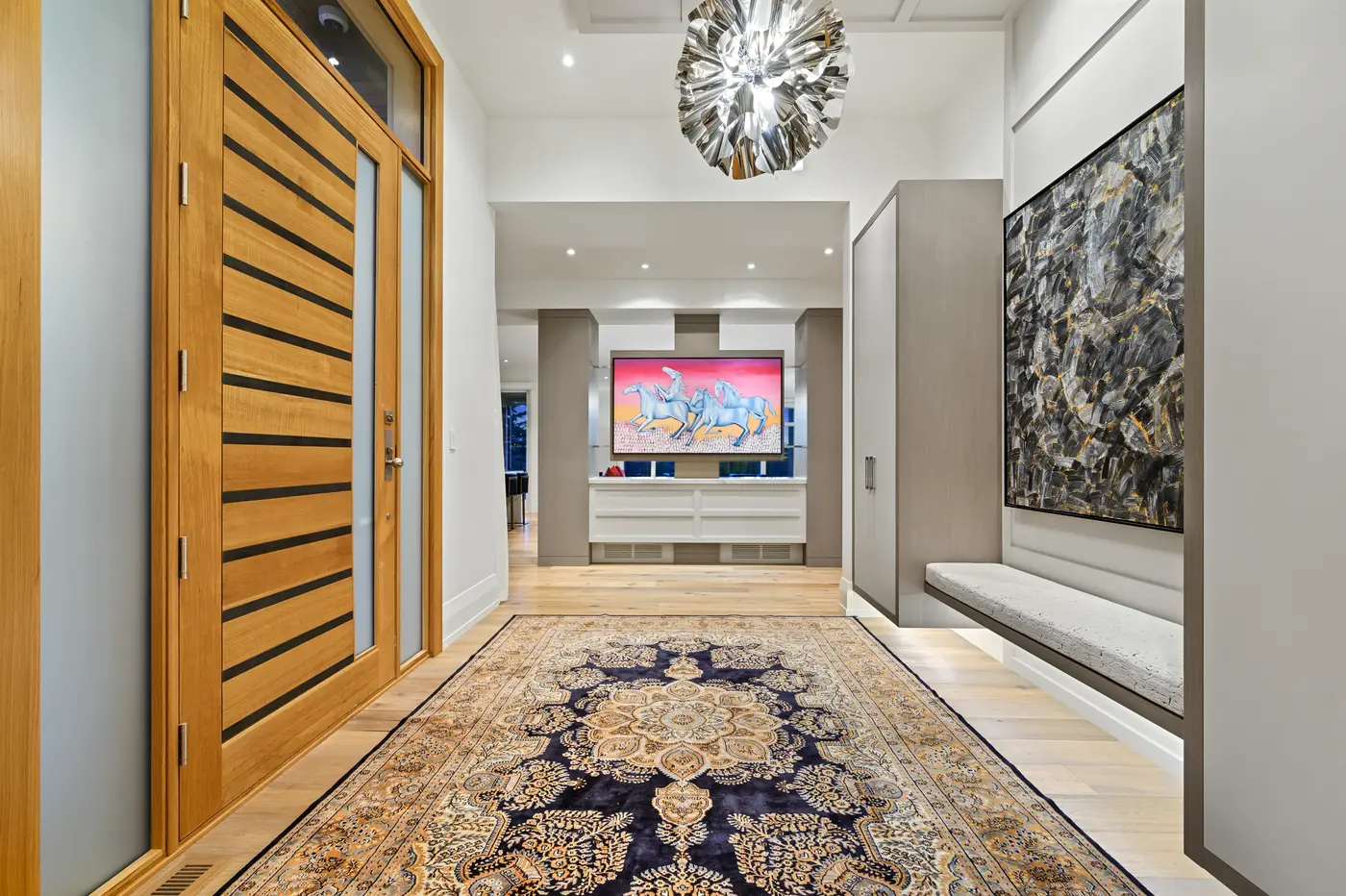 Looking from the front door across the medallion rug to a gallery-like axis where a pink-skied horse painting crowns a white credenza and a floating bench waits beneath textured art.