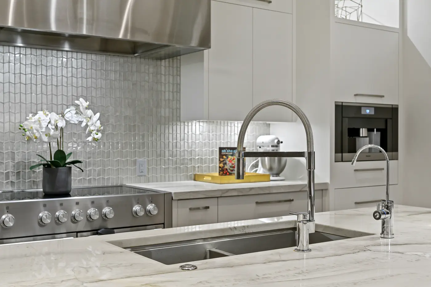 A close vignette of the island's spring faucet with white orchids, the built-in Miele coffee machine and KitchenAid mixer softening the polished kitchen backdrop.