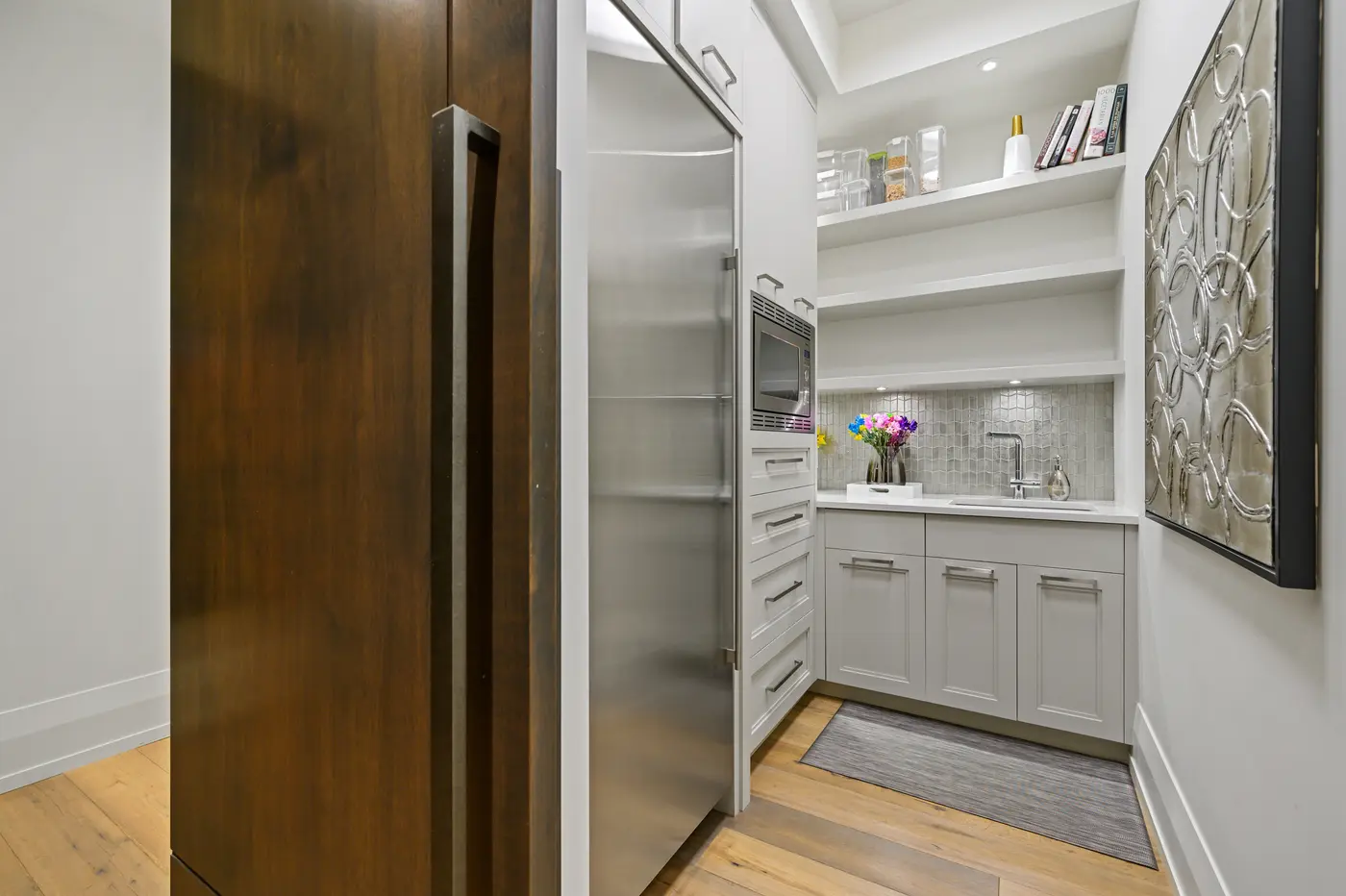 The butler's pantry with a full stainless refrigeration column, built-in microwave, prep sink under iridescent tile, and open shelves keeping cookbooks and canisters at hand.
