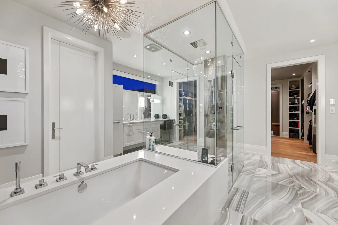 A chrome sputnik chandelier crowns the ensuite's quartz-decked soaker tub and frameless glass shower, with the mirrored vanity wall and walk-in closet visible through the doorway.