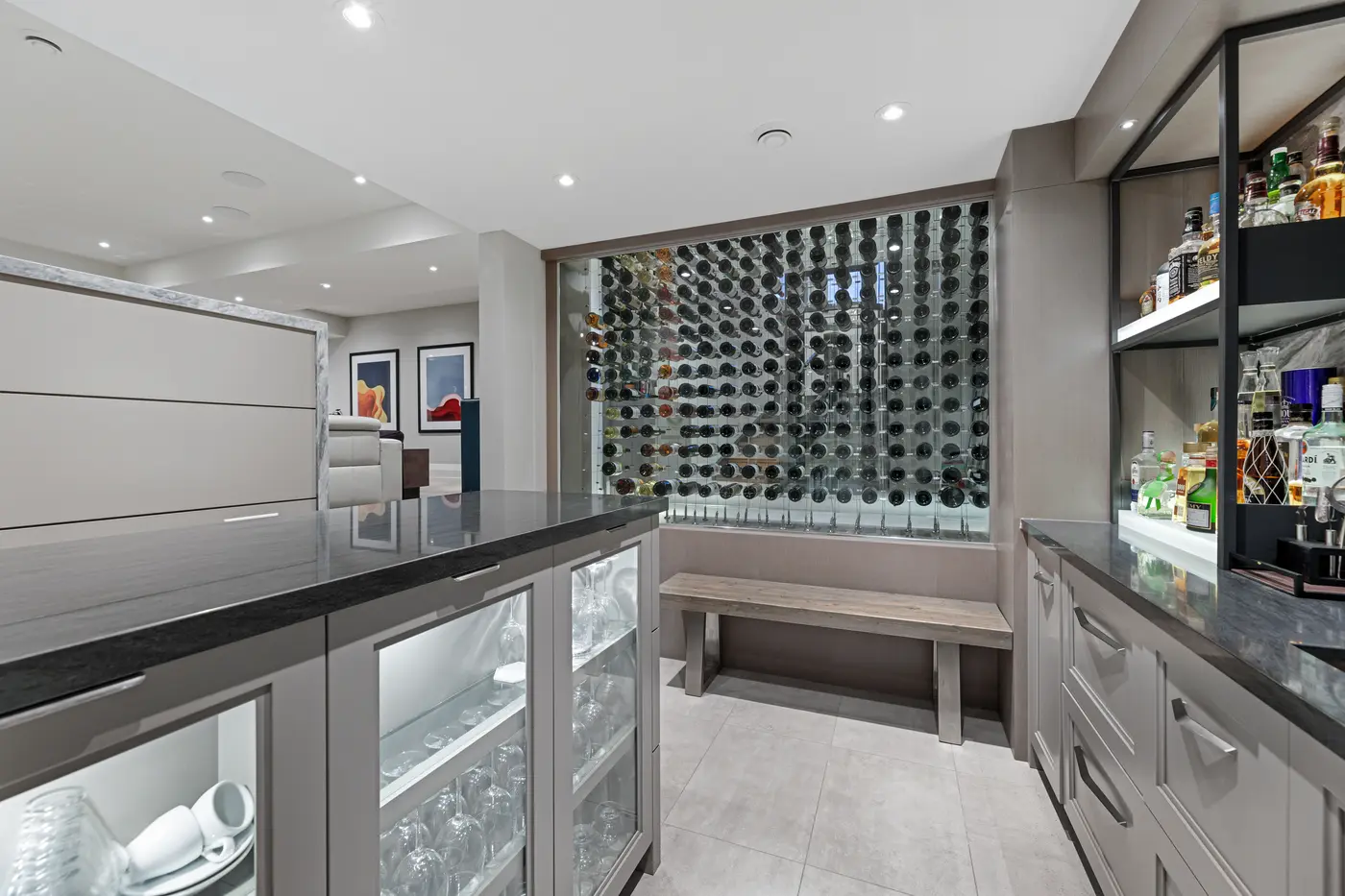 A glass-enclosed, cable-suspended wine display holding hundreds of bottles anchors the tasting room off the lower-level bar, framed by leathered granite counters and illuminated stemware cabinets.