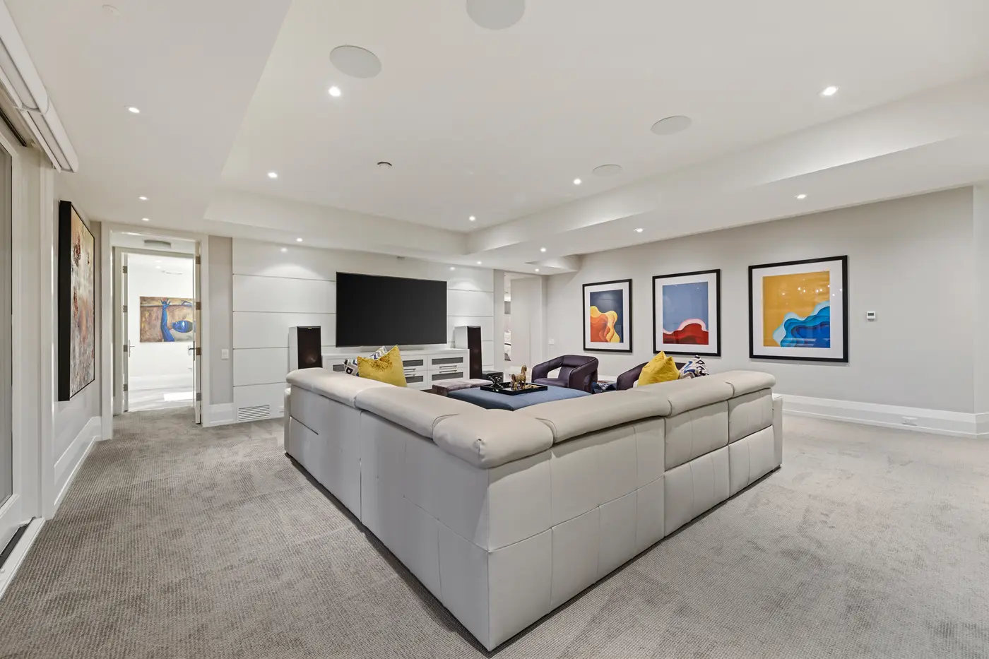 The sprawling lower-level media lounge pairs a plush sectional and tower speakers with a wall-mounted theatre screen and a gallery of vivid contemporary artwork.