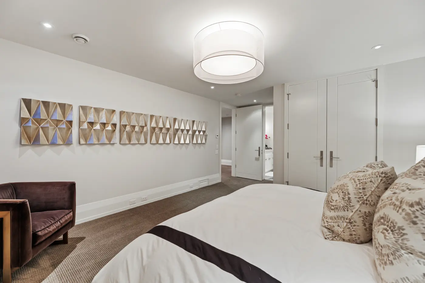 Sculptural gilded relief panels march down the guest bedroom wall toward double closets and an ensuite glimpsed through the open door.
