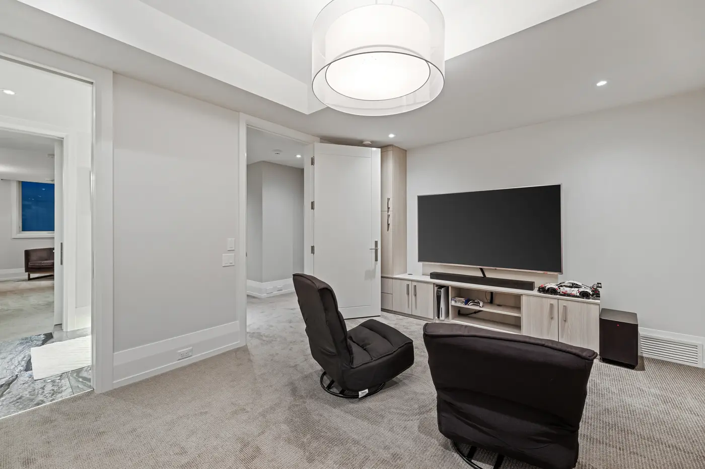 A casual lower-level games lounge with swivel loungers, a wall-mounted screen with soundbar and pale oak built-in cabinetry.