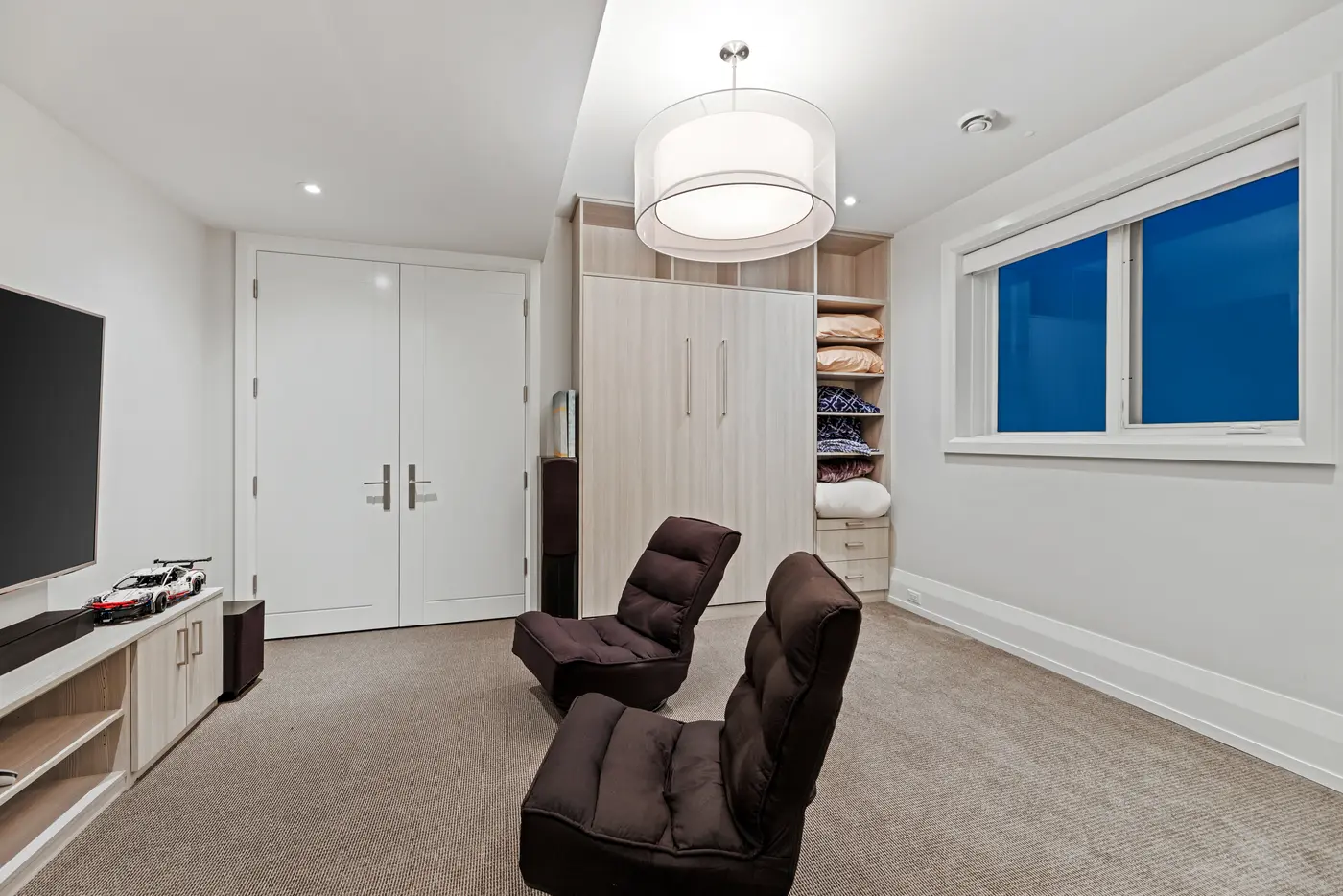 A flexible lower-level suite reveals its concealed Murphy bed cabinetry in pale oak, with floor loungers gathered before the media wall.