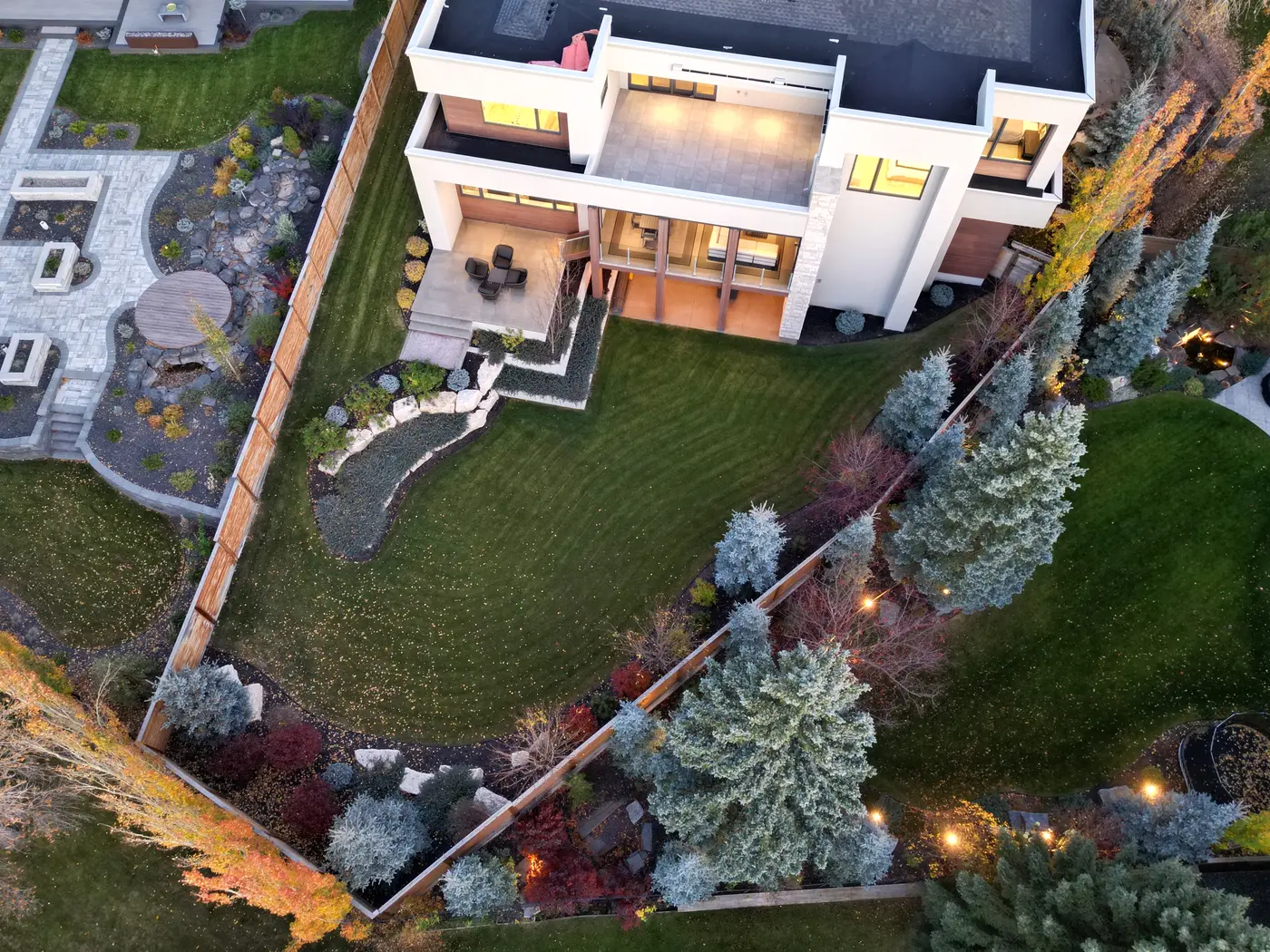 A near-vertical aerial over the property maps the covered outdoor living room, sculpted terraces and evergreen-fringed lawn tumbling toward the landscaped rear boundary.